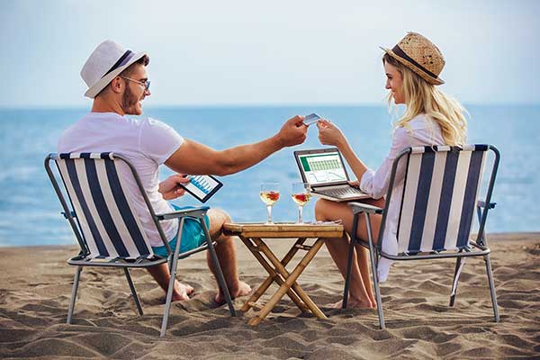 Couple using credit cards on the beach. (Image: Shutterstock)
