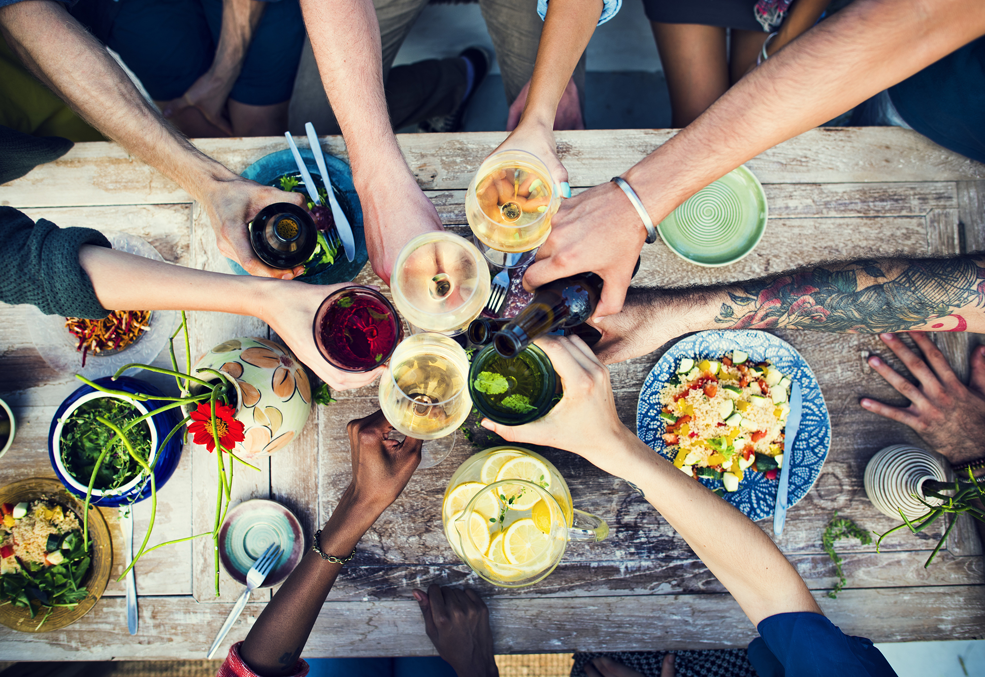People raising glasses on table of food. (Image: Shutterstock)