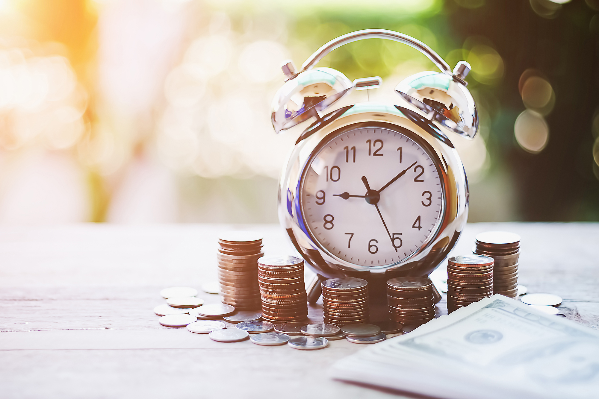 Small clock surrounded by money. (Image: Shutterstock)